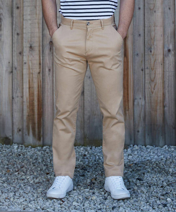 A person is standing on gravel in front of a wooden fence, wearing beige pants, a black and white striped shirt, and Front Row FR621 sneakers, with hands in pockets.