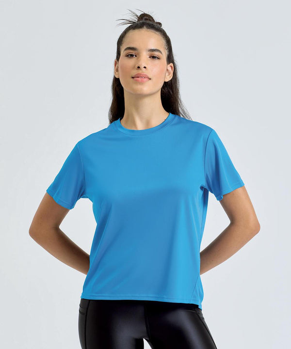 A person stands against a plain light background, wearing the TriDri Women's TriDri Ion-Charge Easy Fit tee in bright blue with black shiny leggings, hands on hips and hair partially tied up.