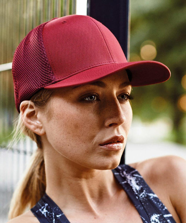 Close-up of a woman wearing a red baseball cap, YP051 by Flexfit By Yupoong, and a dark athletic top, outdoors.