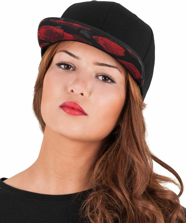 A person with long hair, wearing a black cap with a red pattern on the brim from Flexfit By Yupoong called YP087, looks directly at the camera with a neutral expression.