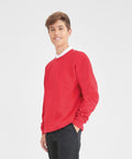 A young person stands smiling and wearing an AWDis Academy AC001 red sweater and black pants.