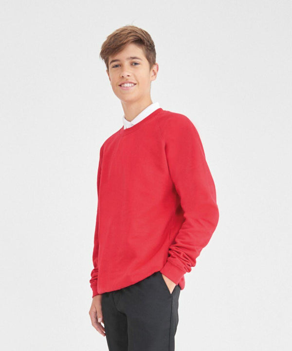A young person stands smiling and wearing an AWDis Academy AC001 red sweater and black pants.