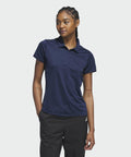A person with braided hair is wearing an adidas AD003 navy-blue polo shirt and black pants, standing with one hand in their pocket, looking slightly to the side.