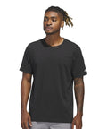 A man with medium-length, blonde-tipped dreadlocks stands slightly sideways against a white background, wearing an adidas Blank tee in plain black and light grey trousers.