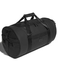 The adidas 1st tee duffle (26L) is a black cylindrical bag with two handles, a shoulder strap, and several zippered compartments, displayed on a white background.