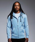 A person with long dreadlocks is wearing an Anthem AM002 light blue zip-up hoodie over a white t-shirt. They are standing against a plain grey background and looking directly at the camera with a neutral expression.