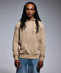 A person with long hair wearing an Anthem AM006 hoodie and blue jeans stands against a plain gray background.