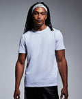 A man with long dreadlocks stands against a neutral background. He is wearing a plain white T-shirt and black pants. A white bandana with a patterned design, Anthem's AM012, is tied around his forehead. He is looking directly at the camera with a calm expression.