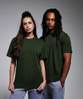 A woman and a man stand side by side, both wearing dark green Anthem AM015 T-shirts and light gray sweatpants. The woman has long, dark hair and the man has long dreadlocks. They both face forward with neutral expressions against a plain, gray background.