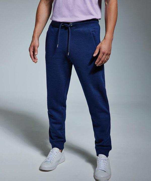 A person wearing a light pink AM030 t-shirt from Anthem, dark blue jogger pants with a drawstring, and white sneakers stands against a plain background with arms relaxed at their sides. The face is not visible in the image.