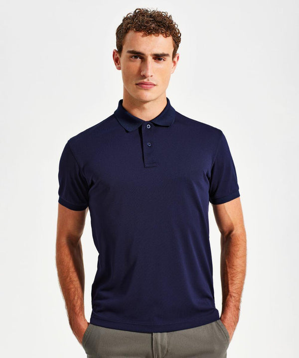 A man with curly hair is standing against a plain white background, wearing a navy blue Asquith & Fox AQ002 and gray pants. His hands are resting in his pants pockets, and he is looking directly at the camera with a slight smile.