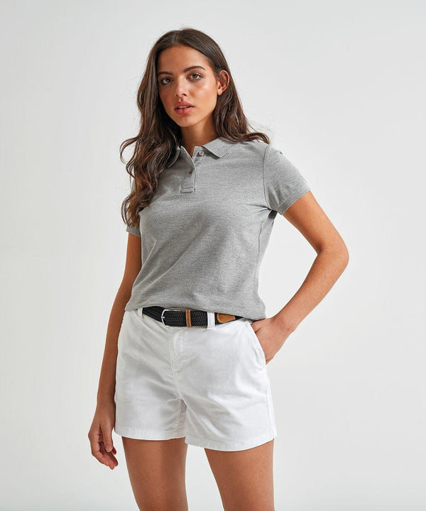 A woman wearing an Asquith & Fox AQ061 grey polo shirt and white shorts stands with one hand in her pocket against a plain background.