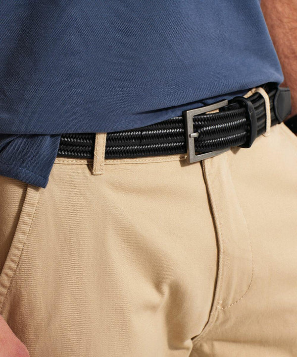 A person wearing a navy blue shirt tucked into beige trousers with an Asquith & Fox AQ903 black braided belt. The focus of the image is on the belt and the waistband of the trousers. The person's arms and hands are partially visible.