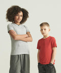 Two kids stand against a light background. The child on the left wears a grey AWDis 150 Kids T and has curly hair; the child on the right wears a red AWDis 150 Kids T and has short, straight hair.