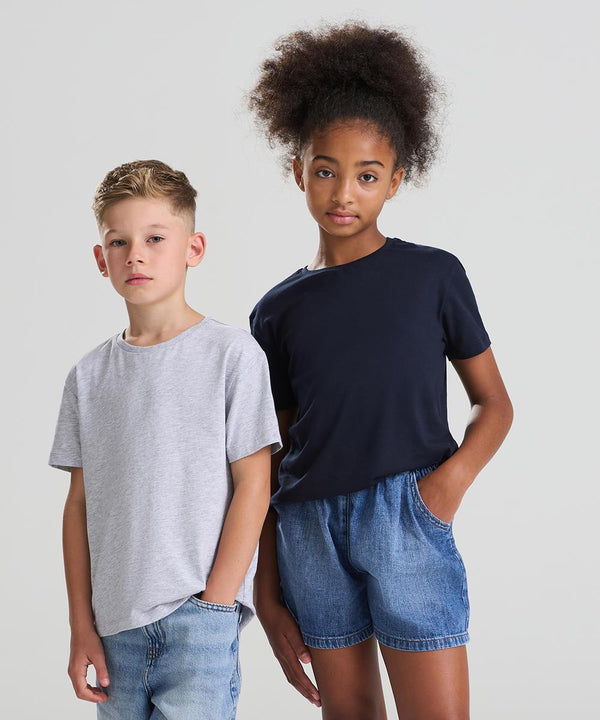 Two children stand side by side against a plain background. The boy on the left wears the AWDis kids 180 T in light grey and denim shorts. The girl on the right wears a navy AWDis kids 180 T and denim shorts, with one hand in her pocket.