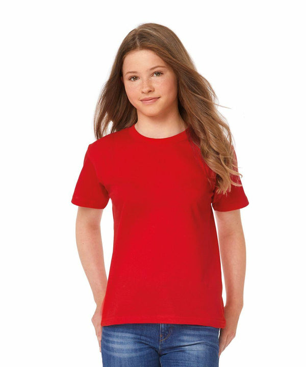 A young person with long, straight hair is wearing a plain red B150B by B&C Collection and blue jeans. They are standing against a white background and looking directly at the camera.