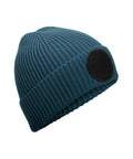 A blue ribbed knit beanie with a folded brim and a large black circular patch on one side, displayed on a white background.