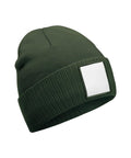 A dark green beanie knitted hat with a folded brim and a blank white rectangular patch on the front, shown against a white background.