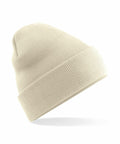 The Beechfield B375R beige knitted beanie, featuring a folded brim, is displayed against a plain white background. It is positioned slightly to the side, highlighting its textured and ribbed pattern.
