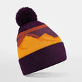 The Beechfield B395R is a knit beanie in purple and yellow, featuring a sunset mountain design and topped with a pom-pom.