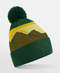 A Beechfield B395R beanie with a pom-pom on top featuring a mountain landscape design in brown and yellow hues. The mountain pattern wraps around the middle section of the hat. The beanie has a folded cuff at the bottom. The background is plain white.