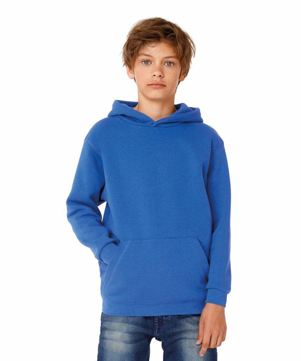 A young person with light brown hair is wearing a blue B420B hoodie by B&C Collection and blue jeans. They have their hands in the front pocket of the hoodie and are standing against a plain white background, looking straight ahead.