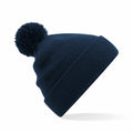 A Beechfield B426B blue knit beanie, featuring a large pom-pom on top and a folded brim, is positioned against a white background.