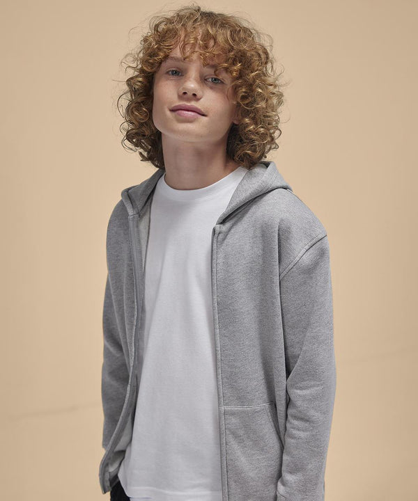 A young person with curly blond hair wears a B&C Collection B&C ID.334 zip hoodie /kids in light grey over a white T-shirt, standing before a plain beige background.