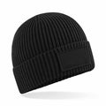 A Beechfield B442R black ribbed knit beanie featuring a blank rectangular patch on the front.