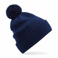 A Beechfield B450N knit beanie in navy blue, complete with a large matching pom-pom on top, is showcased against a white background. The beanie includes a wide, folded brim for enhanced warmth.