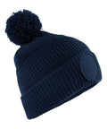 Beanies: Navy blue knitted beanie hat featuring a large pom-pom on top and a circular patch on the front, shown against a white background.