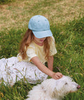 A child in a Beechfield Junior low-profile vintage cap sits in tall grass, reaching out to stroke a white dog nearby.