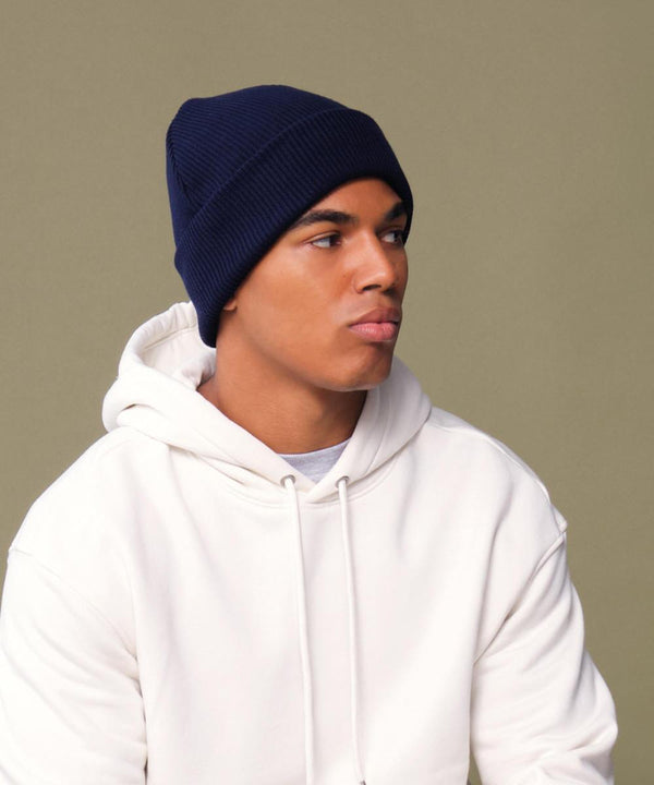 A person wears the Beechfield Organic Cotton Original Cuffed Beanie in navy blue with a white hoodie, looking to the side against a plain, neutral background.