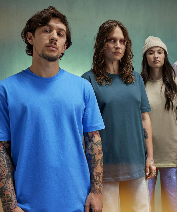 Three people face the camera. The person on the left wears a blue B&C Collection B&C #E220 t-shirt, the centre person has a teal version, and the rightmost wears a beige one with a knitted beanie.