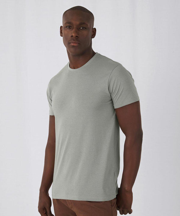 A man with a shaved head is standing against a plain background. He is wearing a B&C Collection BA118 light gray short-sleeved T-shirt and brown pants. His expression is neutral, and he is looking slightly to the left.