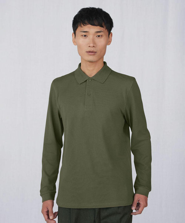 A person with short black hair is wearing a long-sleeve, olive-green BA262 polo shirt by B&C Collection. They are standing against a plain, light gray background, looking directly at the camera with a neutral expression.