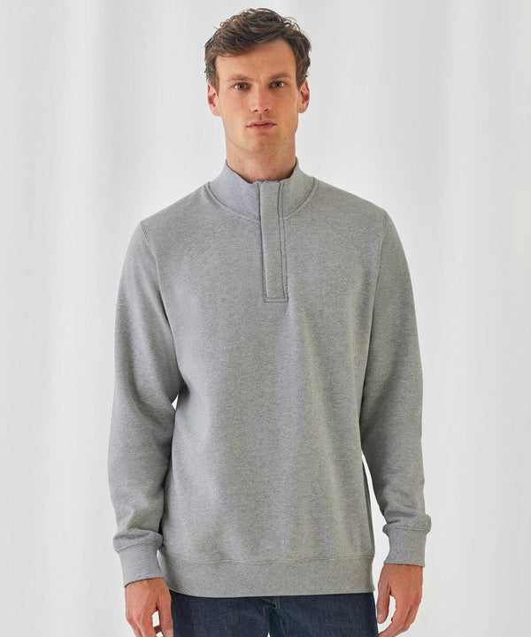 A man with short hair is wearing a light gray B&C Collection BA406 quarter-zip pullover sweater with dark blue jeans, standing against a plain white background. He is looking directly at the camera with a neutral expression.
