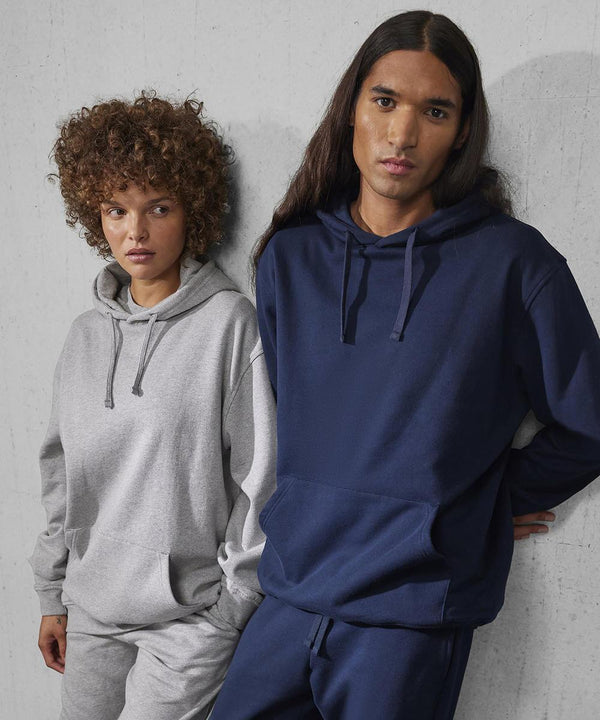 Two people stand against a light grey wall, both with hands in their pockets and neutral expressions. One wears a light grey B&C Collection B&C ID.333 hoodie and trousers; the other wears the same set in navy blue.