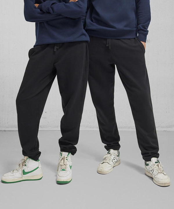 Two people stand side by side in navy sweatshirts, B&C Collection B&C ID.000 joggers, and white trainers with green accents against a plain light grey background. Their faces are not visible.