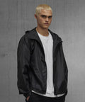 A young person with short bleached blond hair wears a white T-shirt and the B&C Collection B&C #Reset windcheater, standing in front of a grey concrete wall and looking directly at the camera.