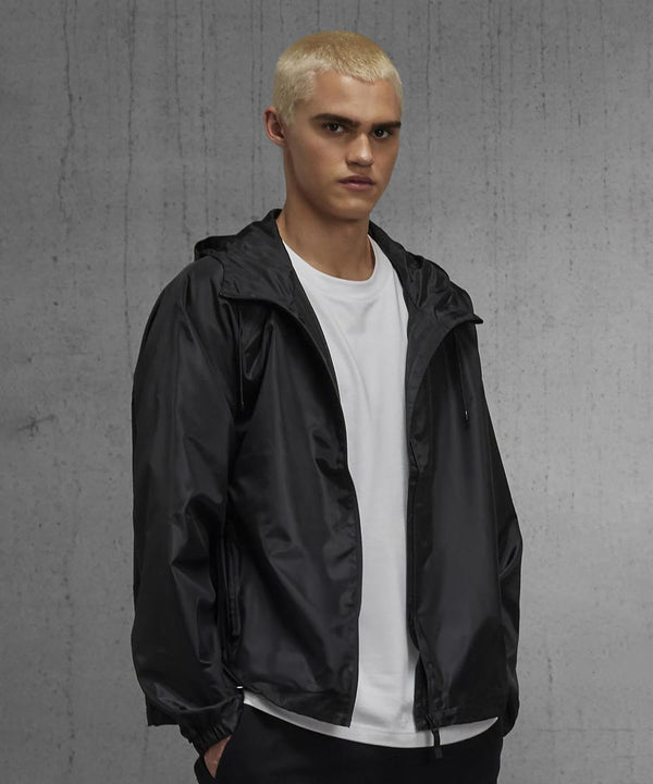 A young person with short bleached blond hair wears a white T-shirt and the B&C Collection B&C #Reset windcheater, standing in front of a grey concrete wall and looking directly at the camera.