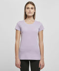 A woman with straight, long hair wears a fitted lavender short-sleeve t-shirt (BB012 by Build Your Brand Basic) and black pants. She stands against a plain white background, facing forward with a neutral expression.