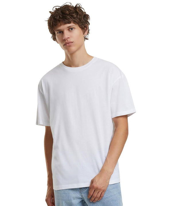 A person with short, curly brown hair is wearing the Build Your Brand Basic Light basic loose tee and light blue jeans, standing against a white background.