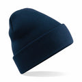 A dark blue BC045 knitted beanie hat from Beechfield, featuring a folded cuff, is showcased against a white backdrop. The hat appears to float at an angle, casting a subtle shadow beneath it.