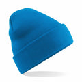 The Beechfield BC045 is a vibrant blue knitted beanie featuring a folded brim, suspended against a white backdrop.