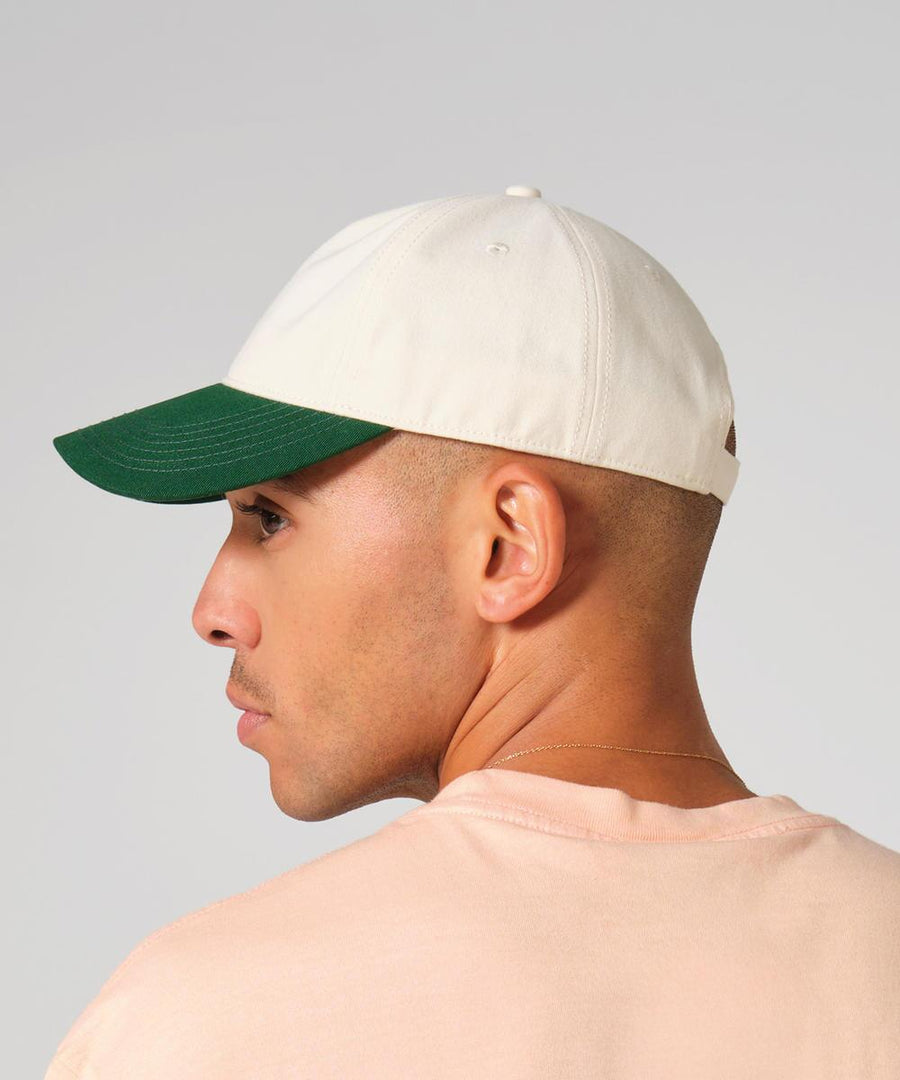 A person wearing the Beechfield Contrast Peak Leisure Cap in cream with a dark green peak and a light pink shirt is seen from the back and side against a plain background.