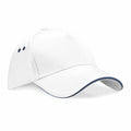 The Beechfield BC15C is a plain white baseball cap featuring a curved brim and two small ventilation holes on each side. The brim's edge is subtly accented with dark blue. The cap is showcased against a white background.
