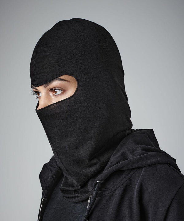 Person wearing a black Beechfield BC225 covering their head and neck, leaving only their eyes exposed. They are dressed in a black hoodie, facing to the left, with a neutral gray background.