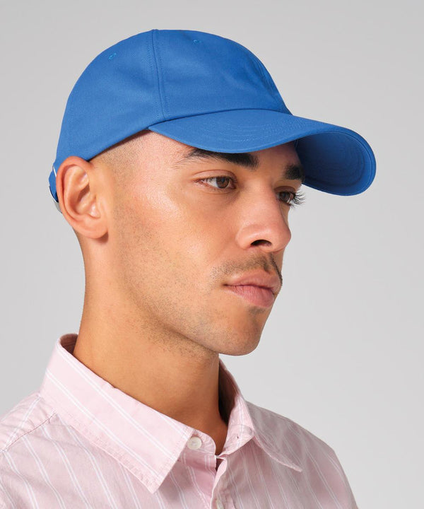A man wearing a Beechfield EarthAware organic cotton studio cap in blue and a light pink collared shirt looks to the side against a plain grey background.