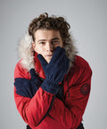 The Beechfield BC296 product features a person with curly hair wearing a red winter jacket with a fur-trimmed hood and blue gloves crossing their arms in front of their chest. The person has a neutral expression and stands against a plain gray background.